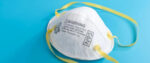 An N95 mask with yellow straps lying on a sky-blue countertop.