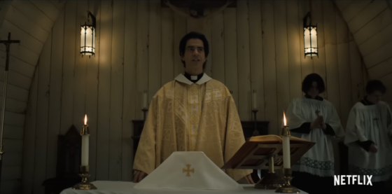 Screenshot from the Trailer for Midnight Mass, featuring a yellow-frocked priest at a humble altar giving a sermon while some altar boys pray behind him