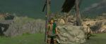 The adventurer Link standing in a hooded scarf next to a large stone well in The Legend of Zelda: Tears of the Kingdom.