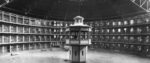 A black and white photo of panopticon, with a central guard tower in the middle of a ring of prison cells.