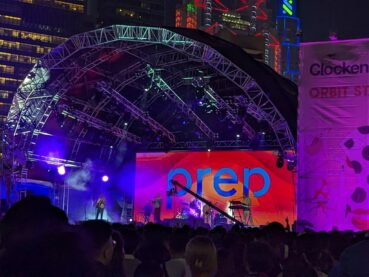 A photo by the author of the band PREP on stage under the half shell and the neon buildings of Hong Kong