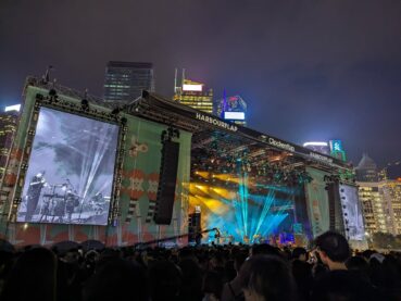 A photo of the band Wang Wen on stage with thousands of festival goers watching the stage and a large screen where a band member plays a trumpet