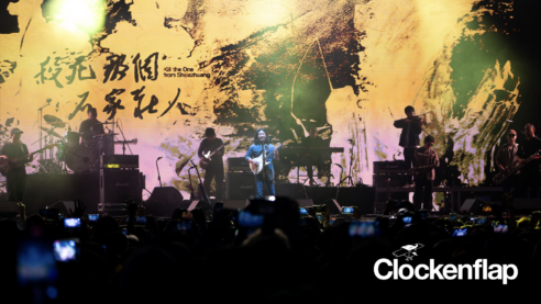 A press photo of Omnipotent Youth Society with at least 9 musicians on stage and the fans documenting every second of it