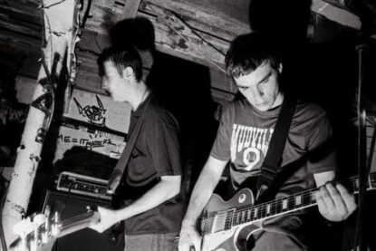 A black and white performance photo of Militarie Gun playing a gig on a small indoor stage.