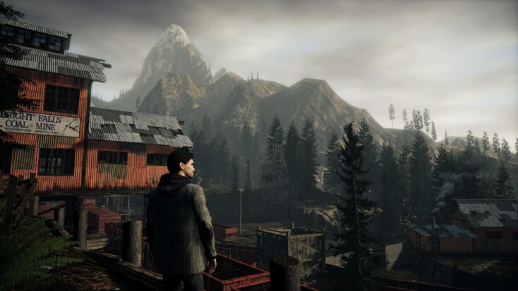 A screenshot from Alan Wake 2 shows the titular character standing next to a decrepit building, gazing moodily out at the surrounding pines and mountains.