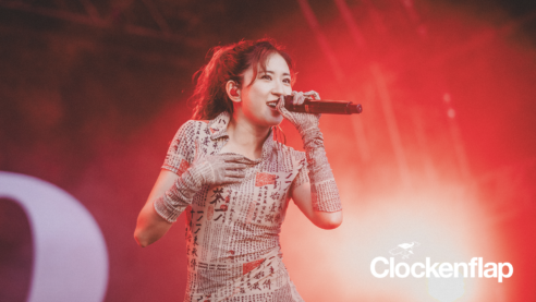 a press photo for 9m88 featuring the singer with microphone in hand wearing an outfit covered in calligraphy, hand on chest, smiling over the crowd