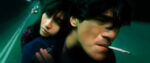 A shot from Wong Kar-wai's Fallen Angels shows a man leaning forward with a cigarette hanging from his mouth while a woman leans tenderly against his back.