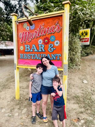 A charming photo of Wife of the Year with her arms around Kids 1 and 2 of the Year standing in front of the colorful and floral Martina's Bar & Restaurant sign.
