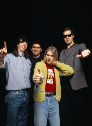 Kurt Cobain stands with Nirvana, the bright yellow of his cardigan and red of his t-shirt standing out against the relatively drab clothing of his bandmates'.