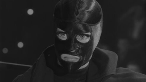 A screenshot from The Panther Woman featuring one of the titular were-panthers in their luchadore mask making their eyes look huge with a very stern look on their face