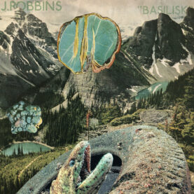 The cover for J. Robbins' Basilisk shows a basilisk emerging from a giant muddy tire in front a mountainous background.