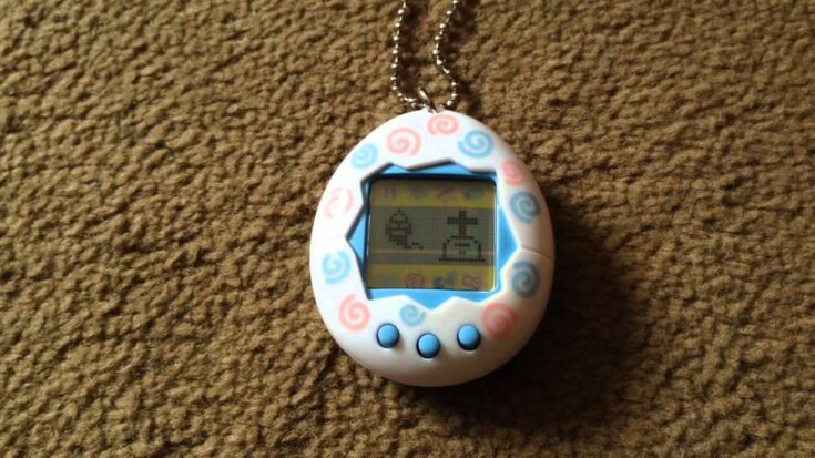 A Tamagotchi lies on a brown carpet, its inhabitant's spirit rising from a pixellated grave.