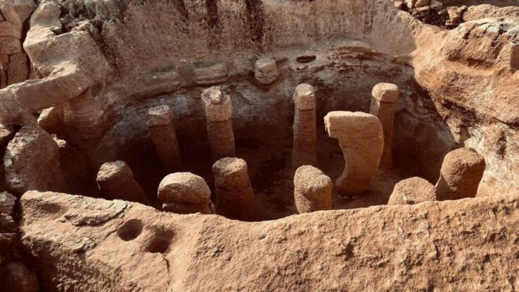A deep pit in the ruins of Göbekli Tepe has a circular arrangement of stone pillars alongside some wall embellishments that resemble humanoid faces.