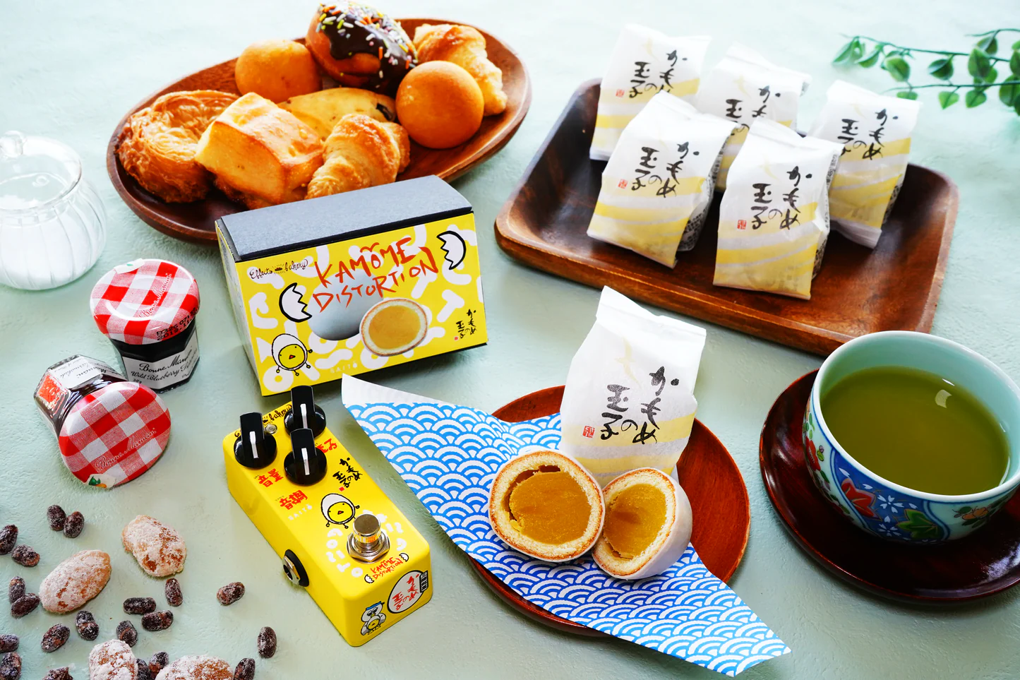 Kamome Distortion, a fried egg-themed effects pedal, is displayed on a table laden with breakfast foods.