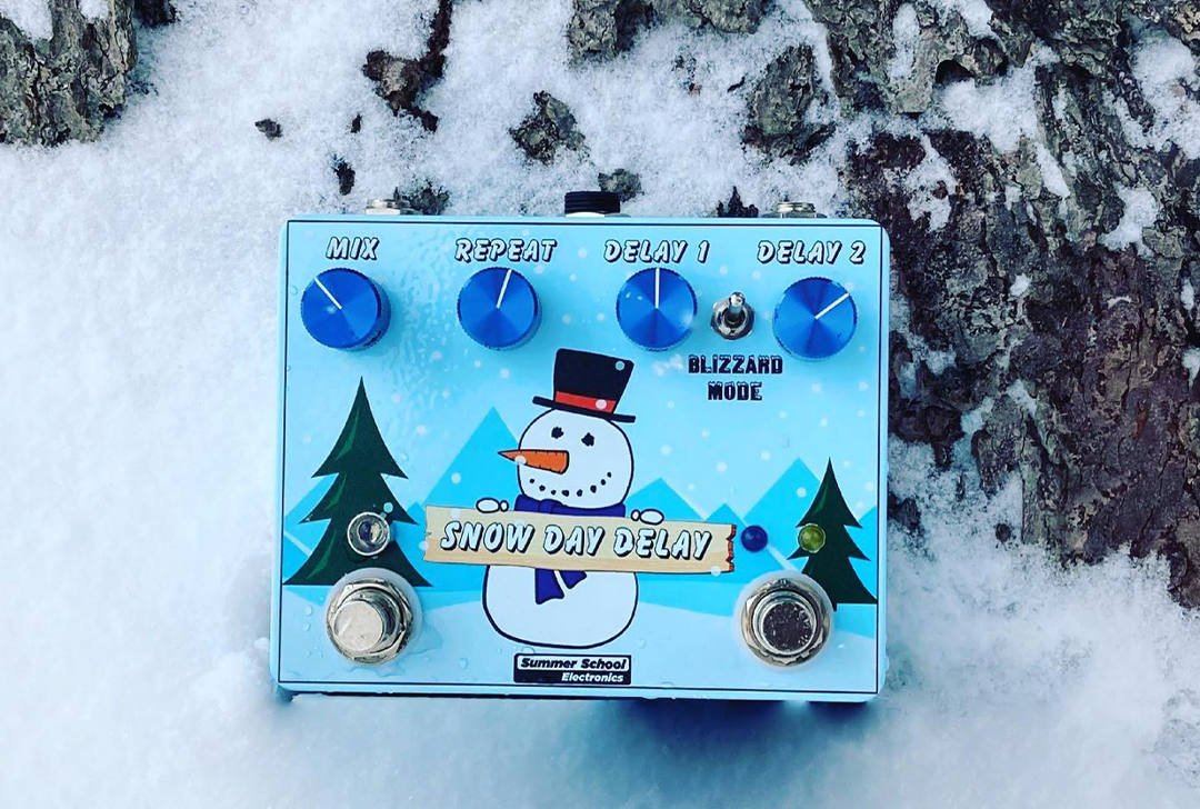 Photographed on a bed of fresh-fallen snow, the Snow Day Delay effects pedal features a smiling snowman holding a sign bearing the pedal's name.