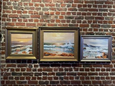 A trio of banksy paintings hanging on a brick wall