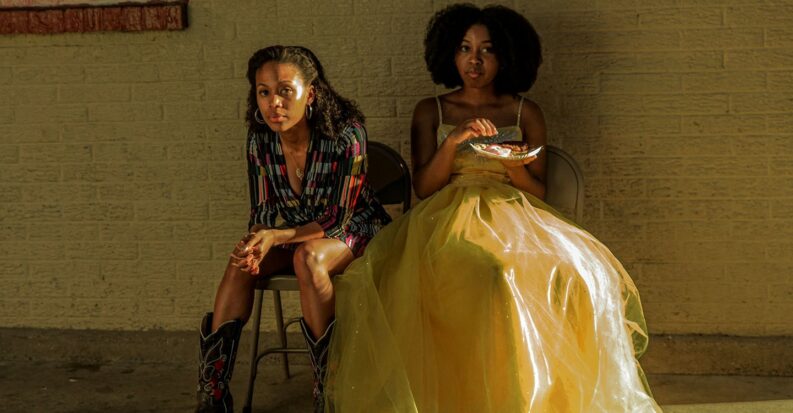 A still from Miss Juneteenth shows a mother and daughter waiting in a nondescript hallway, the daughter dressed in a pageant ball gown and picking at a plate of food.