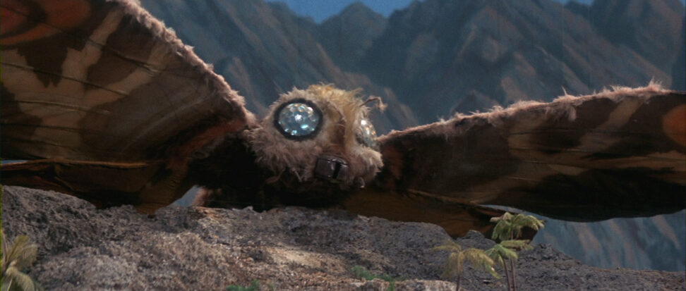 A still from Mothra showing the titular character in flight, her eyes two glittering blue orbs.
