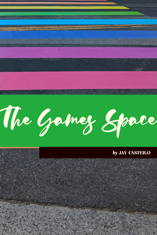 A photograph of a rainbow crosswalk on a paved street. "The Games Space by Jay Castello" is written in a green stripe across the image.