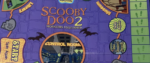 A closeup of the board for Scooby Doo 2 Monsters Unleashed, with a purple layout, comic drawing of the control room, bats, and skulls with peace symbols for eyes for some resaon