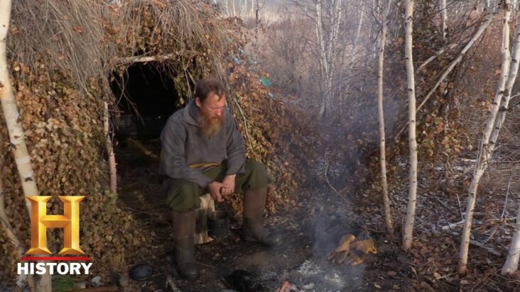 A contestant on the History Channel's Alone sits in the doorway of a makeshift hut he constructed during his time on the show.