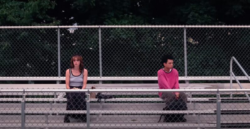 Maddy and Owen sit on empty bleachers at school, together but still about six feet apart.