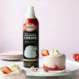 a promo photo featuring an aerosol can of President Whipped Crème nest to a strawberry dessert featuring a perfect dollop of the product.