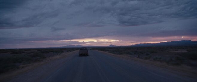 another shot from The Rover of a truck driving down a desert road at sunrise, the landscape bleak and the clouds billowing