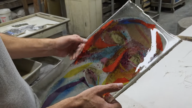 A screenshot from Holy Frit where someone is holding a panel of stained glass that looks like a cubist-ish Picasso face of red, blue and yellow glass