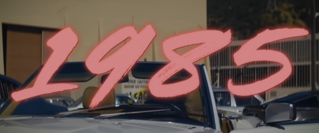 A screenshot from the trailer for Maxxxine with a period correct convertable car and the year 1985 over the image in hot pink 