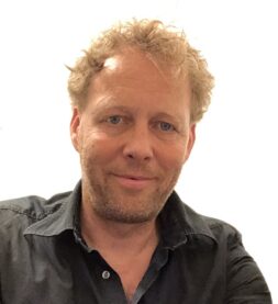 A headshot of theHunter developer Kim Krogh Nielsen, with curly blond hair, a five o'clock shadow, and a wry smile