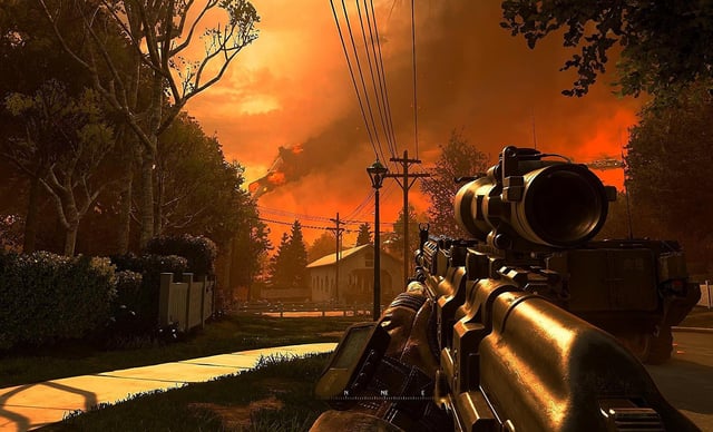 A screencap from the Wolverines level of Modern Warfare 2 shows the player's perspective staring down the eyepiece of a gun at a burning suburban street.