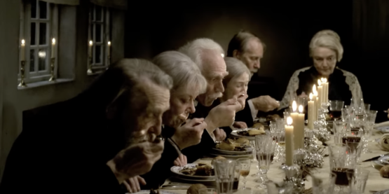 Another screenshot from the trailer for Babette's feast featuring a beautiful table dressed in crystal and white candles with many folks taking their first sip of a truly delicious soup ever in their lives