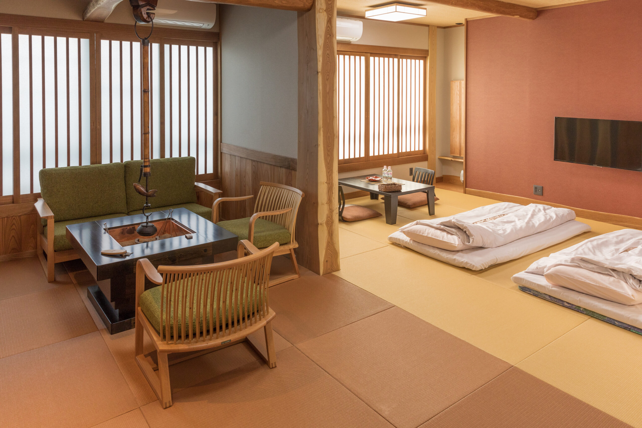 The interior of a ryokan featuring a sitting area with low table in one room and two neatly made-up beds in another.