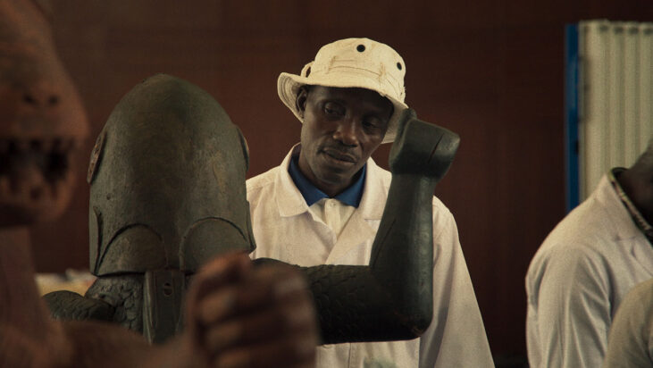 A still from Dahomey shows a man in a bucket hat gazing at one of the stolen artifacts from the Kingdom of Dahomey.