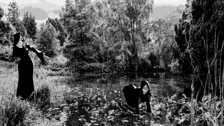 Two nuns in a garden, one searches the ground on her hands and knees while the other stands apart, pointing mid-sentence, as if giving instruction.