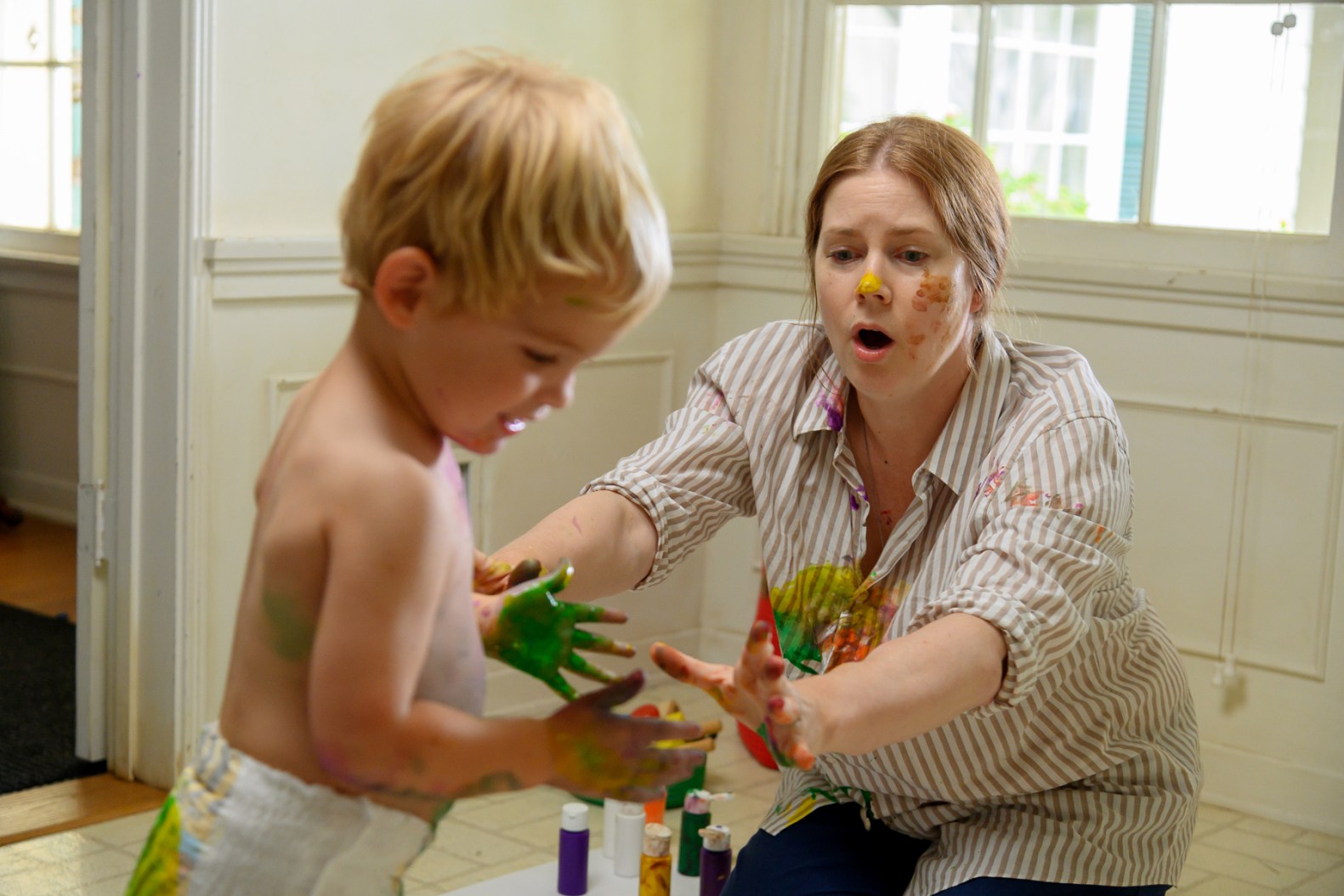 Amy Adams is covered tries to wrangle her child, covered in paint, in a scene from Nightbitch.