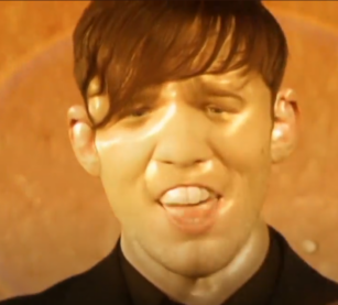 A screenshot from the Everything Everything video with the singer's face puffing out like a balloon animal all yellow and sweaty it's real odd
