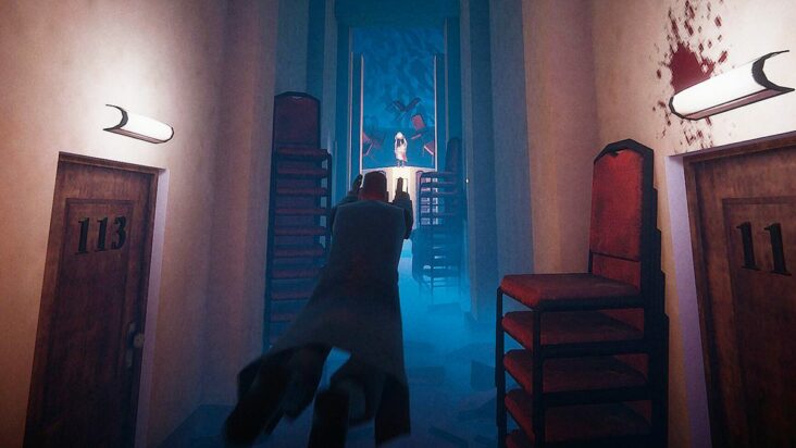 A screenshot from El Paso, Elsewhere shows a man in a long trench coat lunging forwards towards the light of a distant doorway.