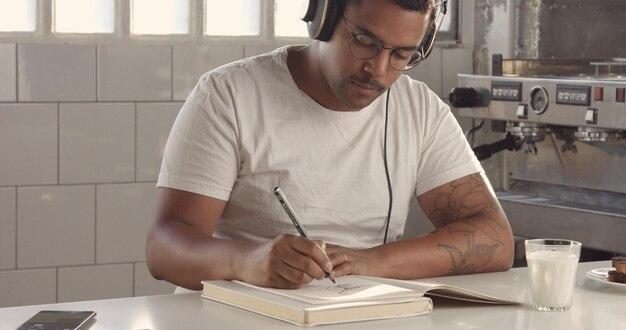 Mixed race man drawing in sunny loft listening music in earphonesimages with sunny flairs