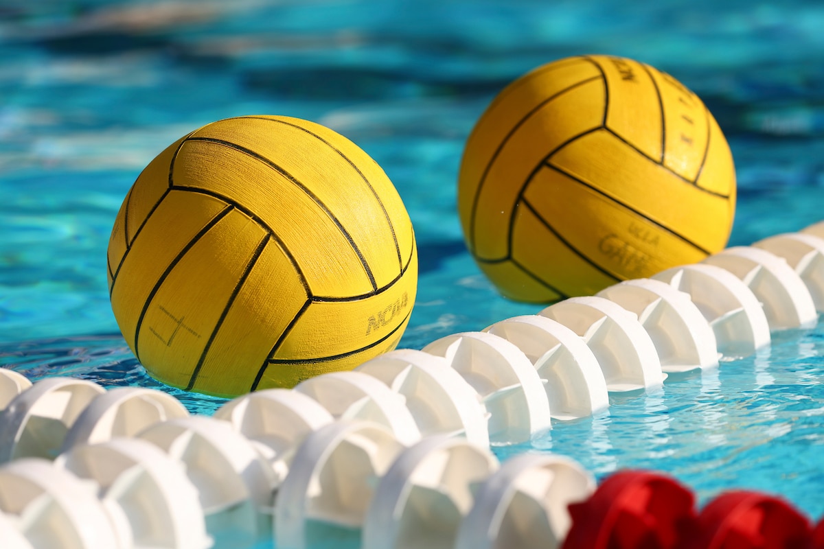 Two water polo balls float next to a rope in an indoor swimming pool.
