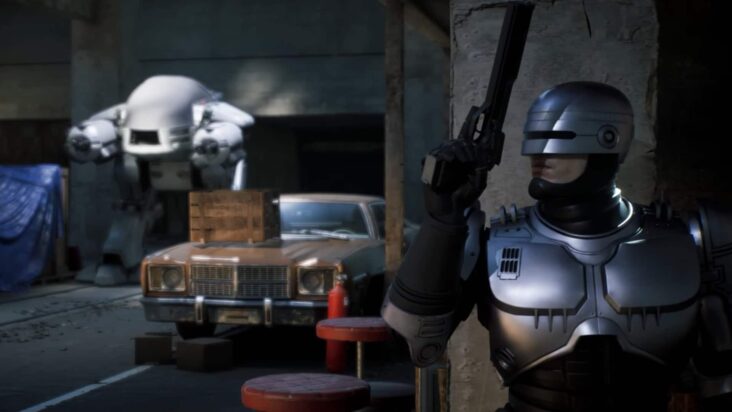 Robocop stands behind a wall, gun drawn, preparing to fight a large mech in a parking garage.