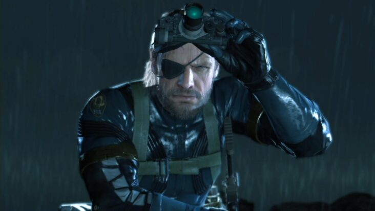 Venom Snake lifts the night-vision goggles from his face in the rain-drenched night.