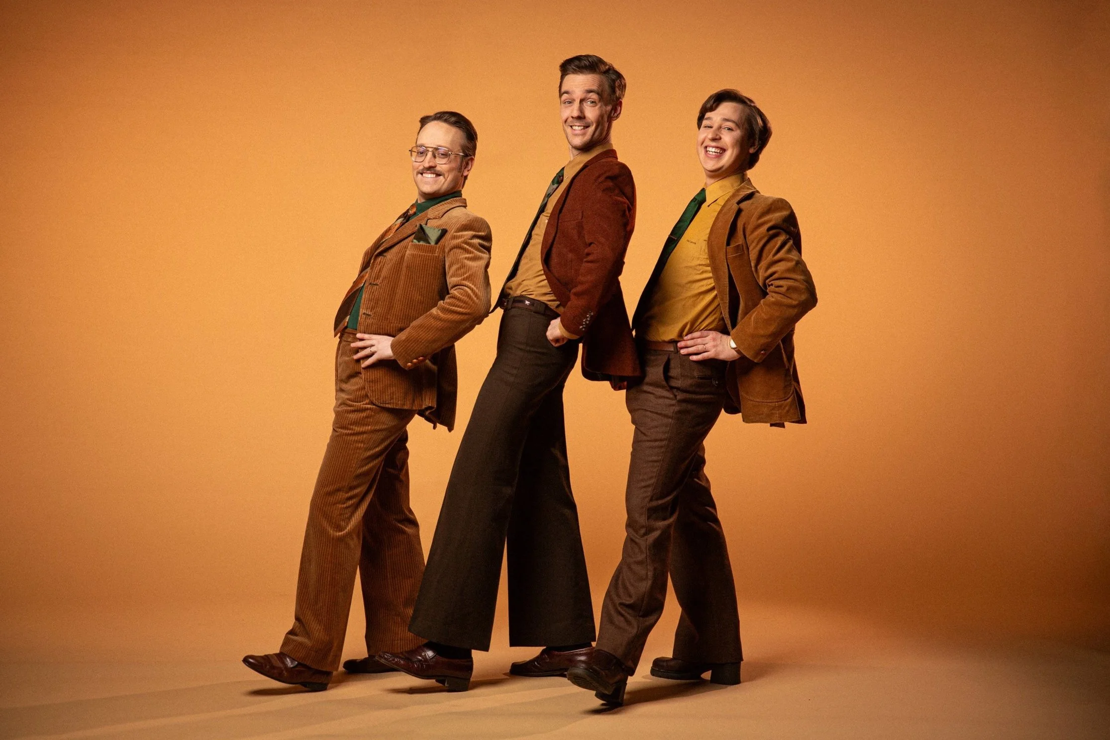 The three boys of KAJ lean back in their brown suits.