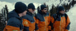 A still from Mountainhead shows the four main characters arm-in-arm in day-glo orange ski coats on the side of a snowy mountain.
