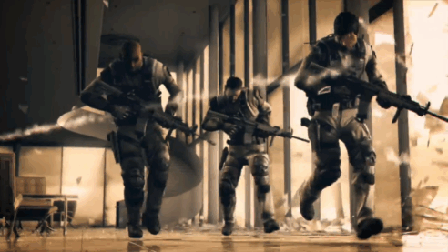 A screenshot from the cinematic trailer for Spec Ops the Line with three soldiers in a sepia-toned urban battle zone running from incoming fire while glass falls around them
