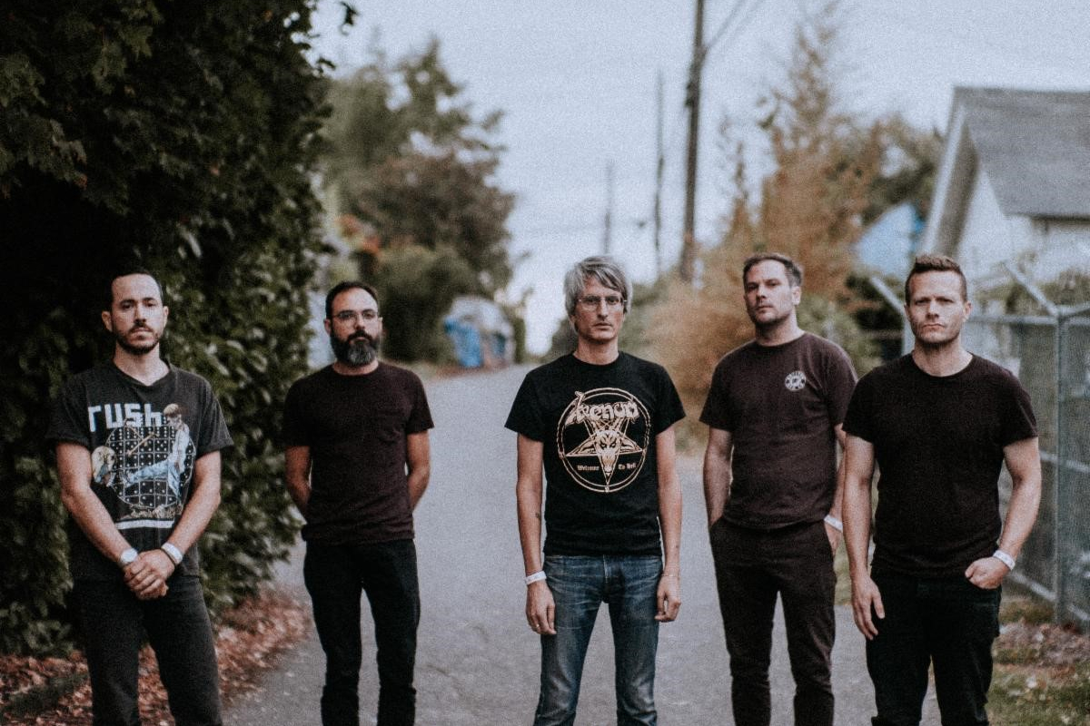 The members of Grails stand in a neighborhood alley, telephone poles and vine-covered fences stretched out behind them.