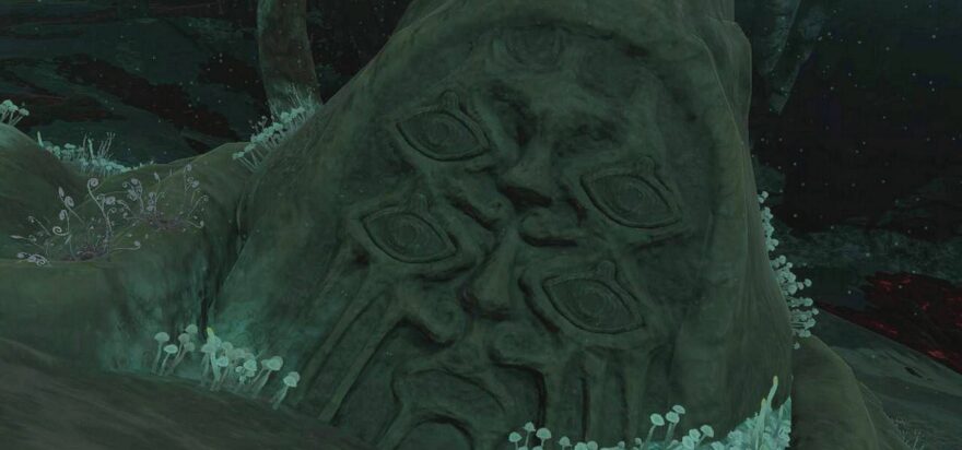 The four-eyed, dual-nosed face of a massive, half-buried statue stares forlornly in this screenshot from Tears of the Kingdom, stone tears carved into its cheeks.