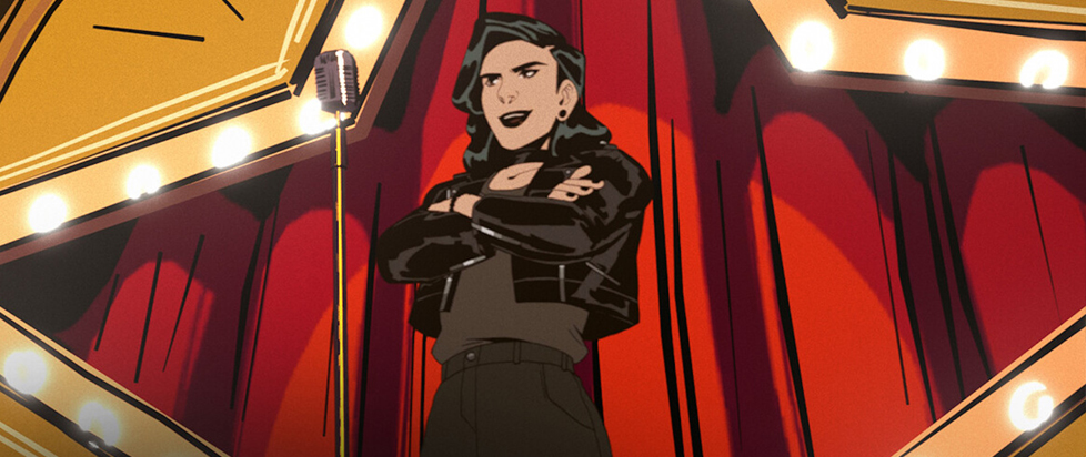A dark-haired woman in a leather jacket stands with her arms crossed in front of a microphone in this screenshot from Stray Dogs, stage lights and bright red curtains behind her.