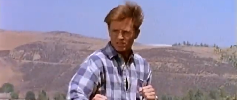 A screenshot from Power Rangers where Blue Ranger billy is out of uniform fighting baddies in a California park in a defensive stance blue flannel and glasses as his blond hair blows in the wind